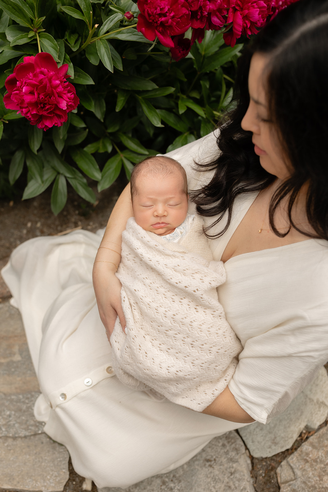 Mother holding her sleeping newborn during an outdoor newborn photography session in Seattle with blooming peonies.