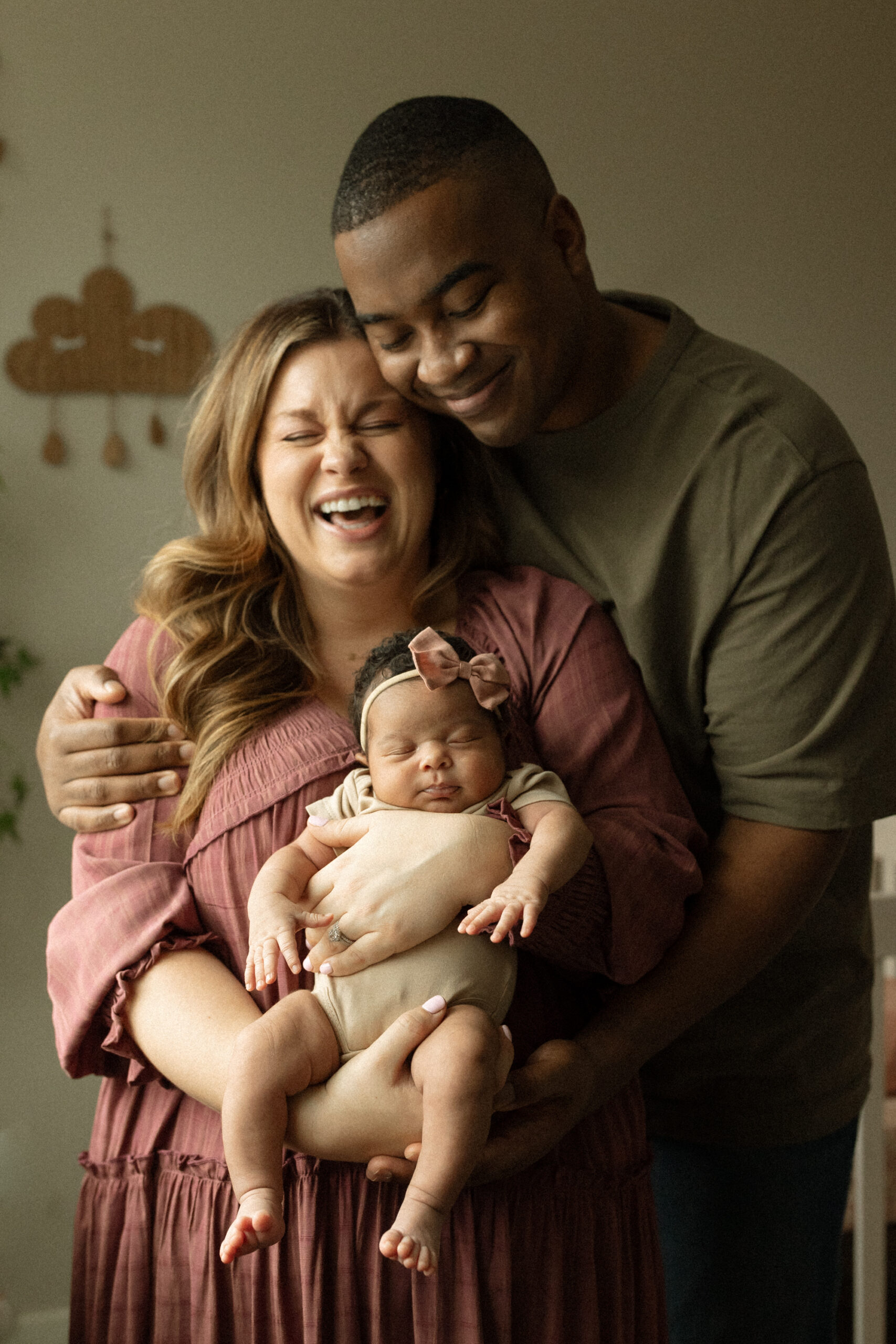 Parents smiling and holding their sleeping newborn during an in-home session.