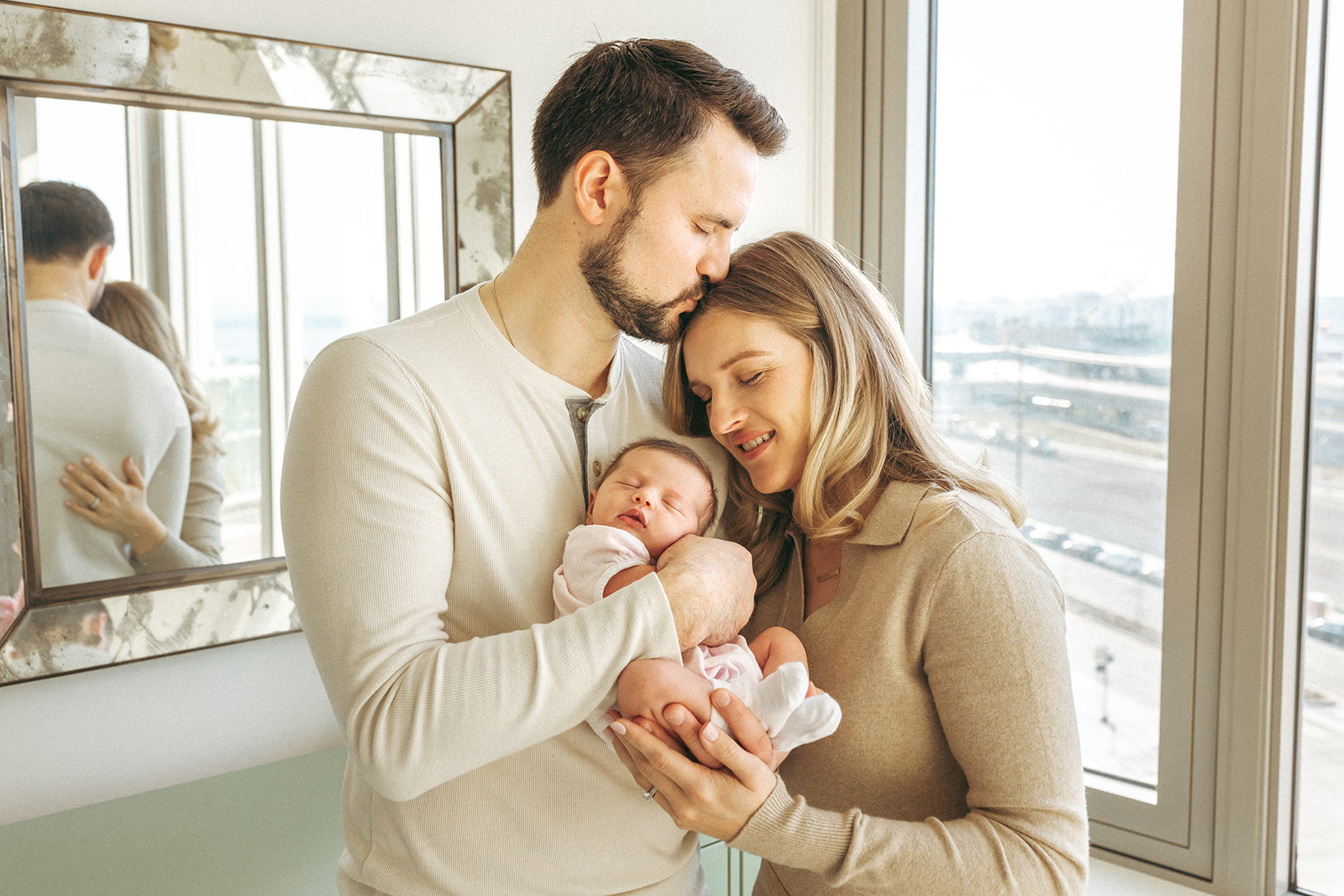 Documentaring parents cuddling their newborn near a bright window at home.